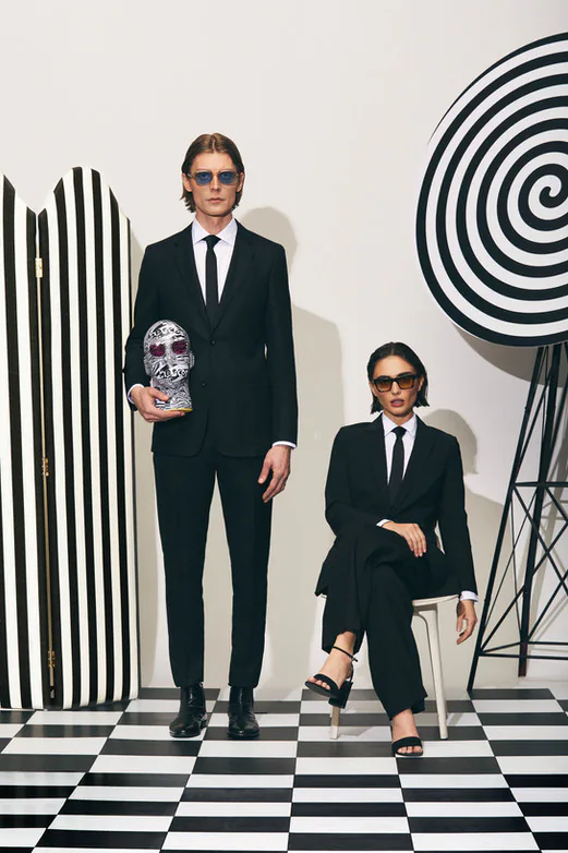 Two models wearing glasses, photographed against an op-art backdrop